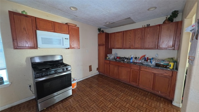 kitchen with dark stone countertops, dark parquet flooring, stainless steel gas range oven, and a textured ceiling