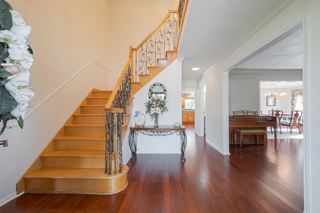 stairway featuring a textured ceiling, a notable chandelier, baseboards, wood-type flooring, and crown molding