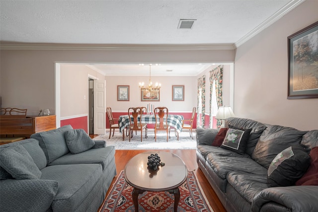 living area featuring visible vents, ornamental molding, a textured ceiling, wood finished floors, and a chandelier