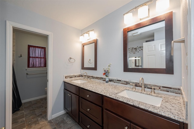 full bathroom featuring double vanity, baseboards, toilet, and a sink