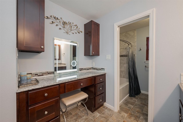 bathroom with tasteful backsplash, shower / tub combo, stone finish flooring, vanity, and baseboards