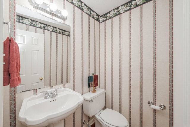 half bath with a sink, toilet, and wallpapered walls