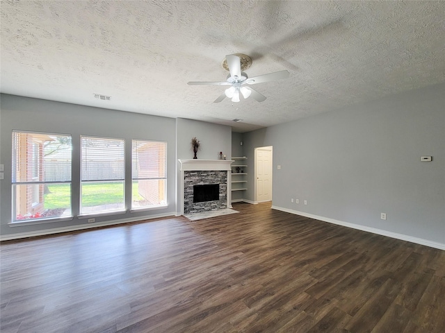 unfurnished living room featuring ceiling fan, dark hardwood / wood-style flooring, a stone fireplace, and a textured ceiling