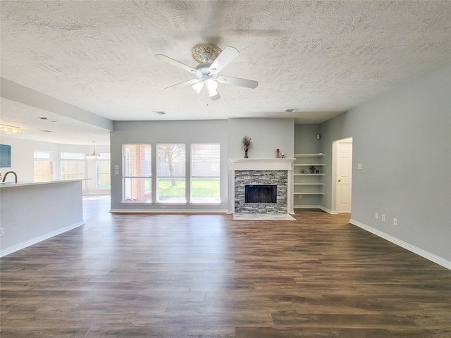 unfurnished living room featuring dark hardwood / wood-style flooring, ceiling fan with notable chandelier, a textured ceiling, and a fireplace