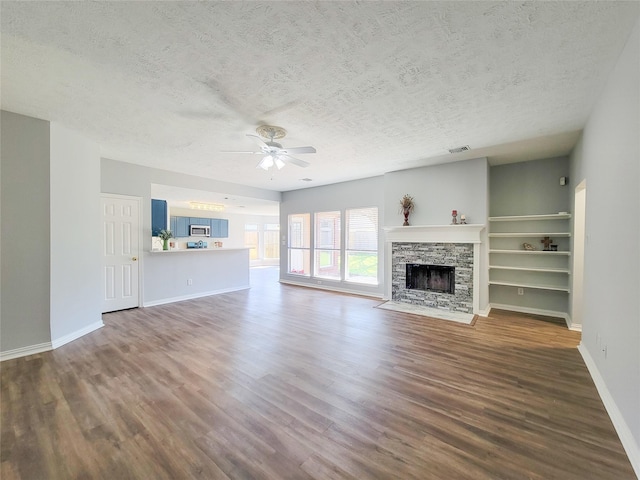 unfurnished living room with a stone fireplace, hardwood / wood-style floors, a textured ceiling, and ceiling fan