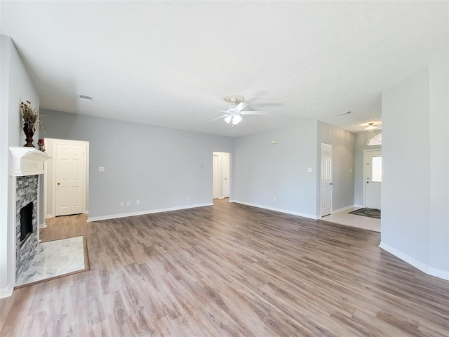 unfurnished living room with a stone fireplace, light hardwood / wood-style floors, and ceiling fan