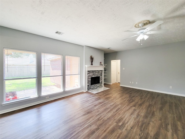 unfurnished living room featuring ceiling fan, a fireplace, dark hardwood / wood-style floors, and a textured ceiling