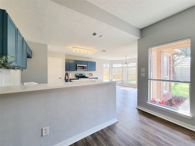 kitchen with blue cabinetry, a chandelier, dark hardwood / wood-style flooring, kitchen peninsula, and stainless steel appliances