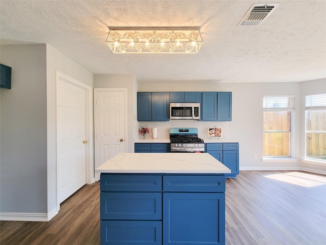 kitchen featuring blue cabinetry, light stone counters, a textured ceiling, dark hardwood / wood-style flooring, and stainless steel appliances