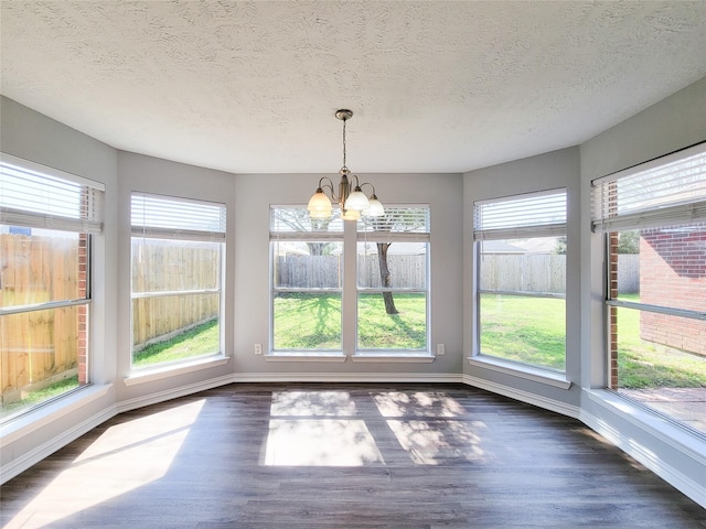 unfurnished dining area with dark hardwood / wood-style flooring, a textured ceiling, a wealth of natural light, and a chandelier