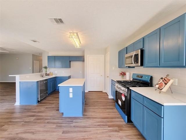 kitchen featuring blue cabinetry, stainless steel appliances, a center island, light hardwood / wood-style floors, and kitchen peninsula