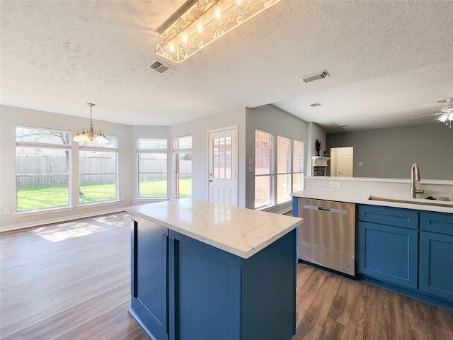 kitchen with blue cabinetry, sink, hanging light fixtures, stainless steel dishwasher, and light stone countertops