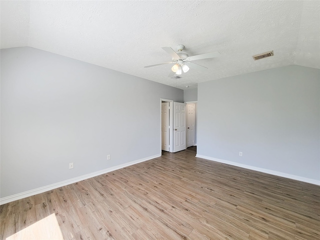 spare room with ceiling fan, lofted ceiling, a textured ceiling, and light hardwood / wood-style floors