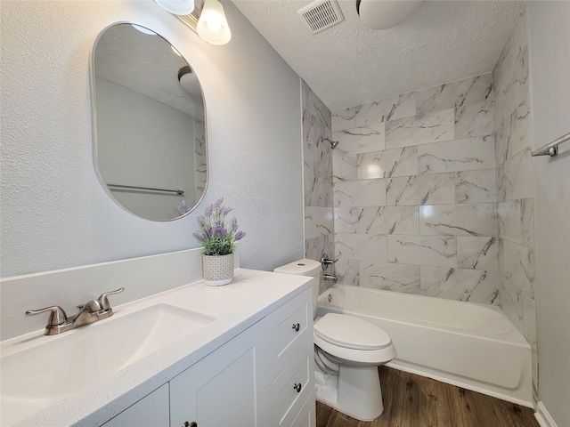 full bathroom featuring wood-type flooring, tiled shower / bath combo, vanity, toilet, and a textured ceiling