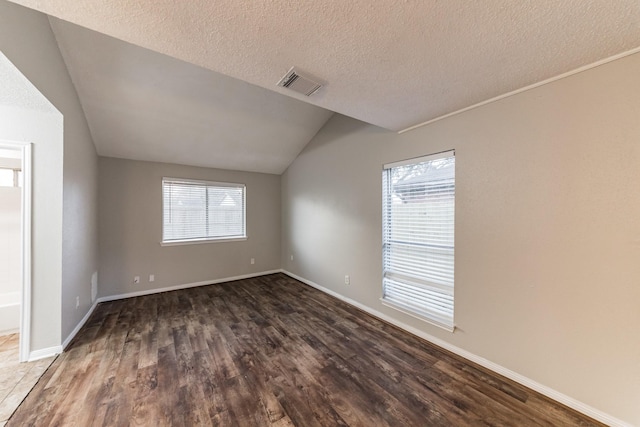 spare room featuring lofted ceiling, dark hardwood / wood-style flooring, and a textured ceiling