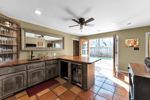 kitchen with dark countertops, a sink, dark brown cabinets, beverage cooler, and a peninsula