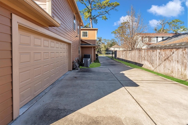 view of side of property with a garage, concrete driveway, fence, and central AC unit