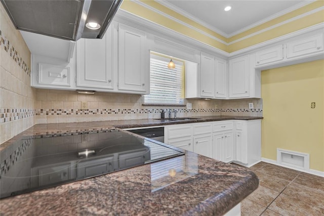 kitchen with wall chimney range hood, white cabinetry, ornamental molding, and a sink