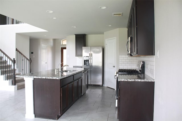 kitchen featuring sink, stainless steel appliances, light stone counters, a center island with sink, and decorative backsplash