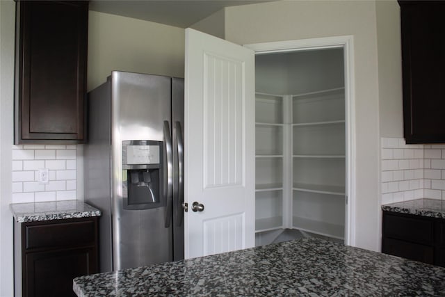 kitchen featuring tasteful backsplash, dark brown cabinetry, stainless steel fridge with ice dispenser, and dark stone countertops