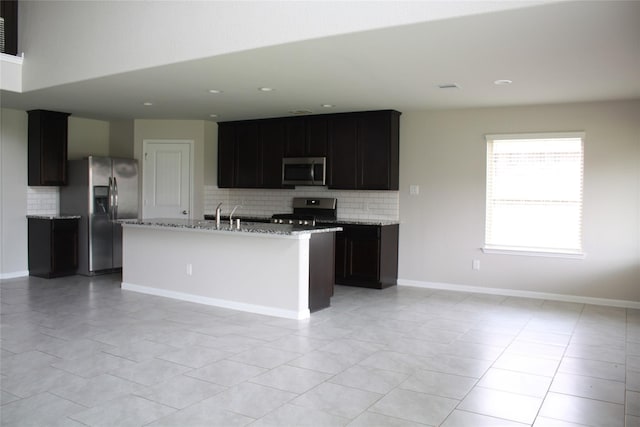 kitchen featuring light stone counters, tasteful backsplash, light tile patterned floors, stainless steel appliances, and a kitchen island with sink