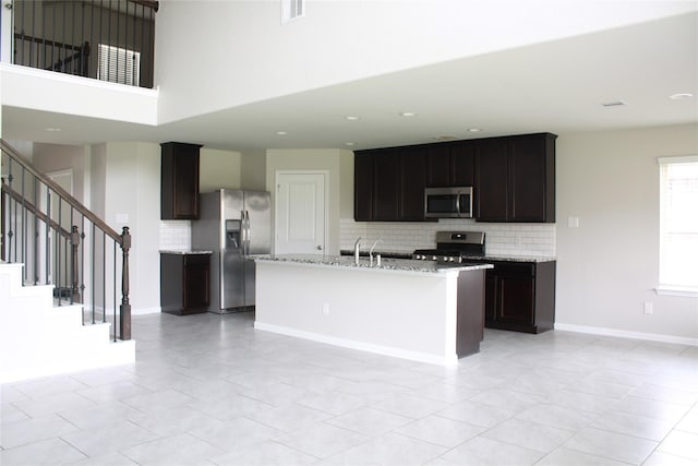 kitchen featuring appliances with stainless steel finishes, a kitchen island with sink, dark brown cabinetry, and decorative backsplash