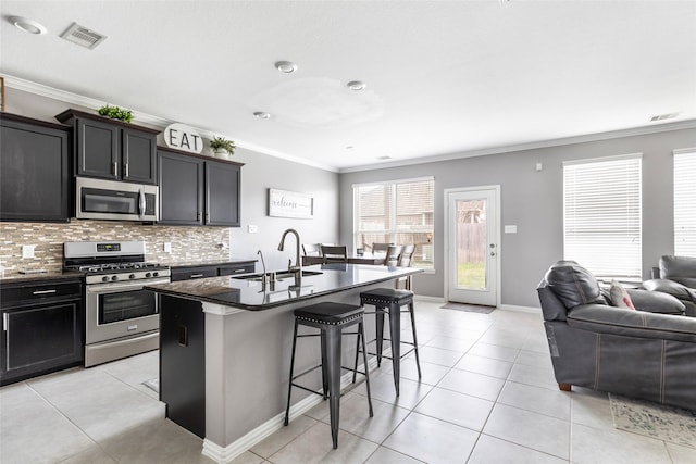 kitchen featuring sink, crown molding, a kitchen island with sink, stainless steel appliances, and a kitchen bar