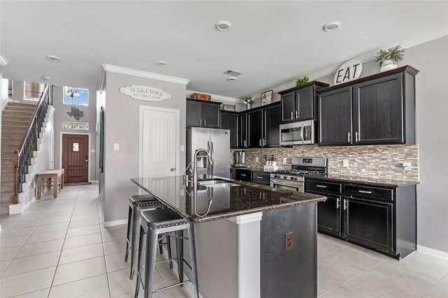 kitchen featuring ornamental molding, appliances with stainless steel finishes, a kitchen island with sink, and dark stone counters