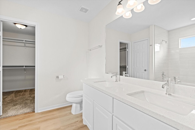 bathroom with hardwood / wood-style flooring, an inviting chandelier, tiled shower, vanity, and toilet