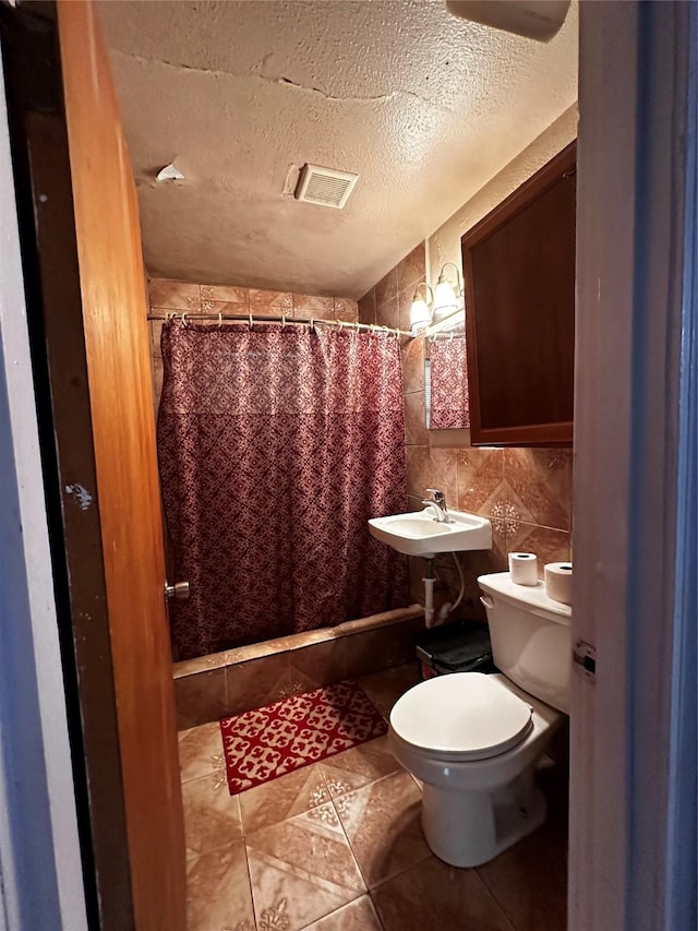 bathroom with toilet, sink, tile walls, a textured ceiling, and tile patterned flooring