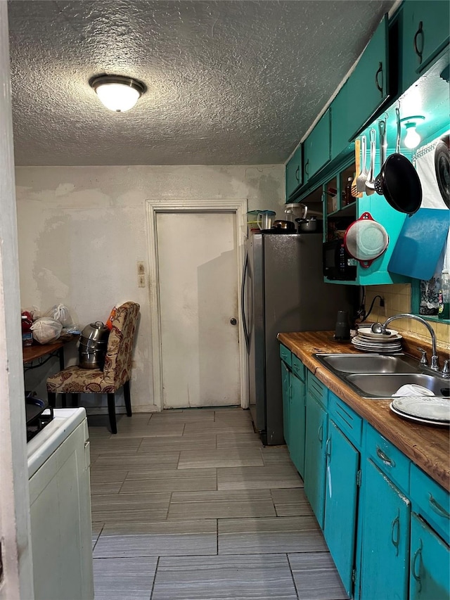 kitchen featuring butcher block countertops, sink, stainless steel fridge, a textured ceiling, and washer / clothes dryer