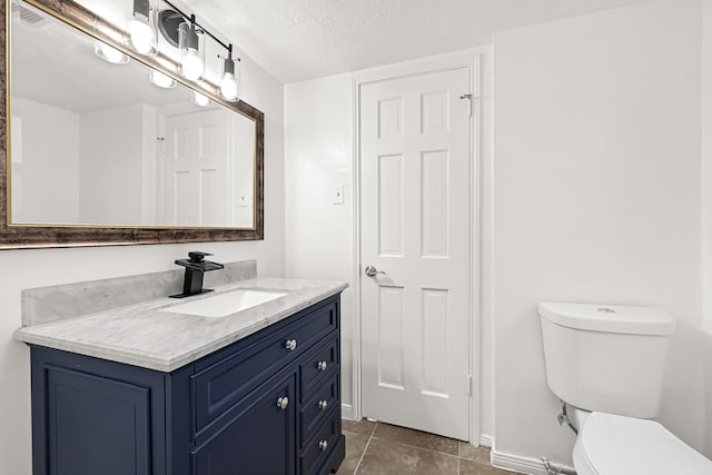 bathroom featuring a textured ceiling, toilet, vanity, baseboards, and tile patterned floors