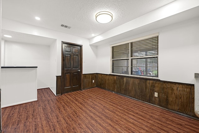 unfurnished room with a textured ceiling, wooden walls, a wainscoted wall, wood finished floors, and visible vents