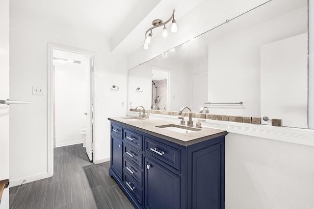 bathroom with double vanity, a sink, toilet, and baseboards