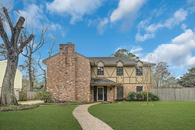 tudor house with brick siding, a chimney, fence, and a front yard