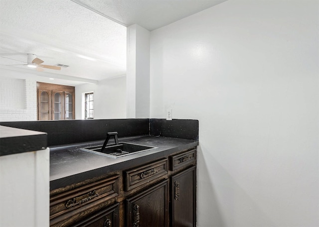 kitchen with dark brown cabinetry, dark countertops, ceiling fan, a textured ceiling, and a sink