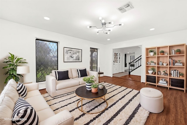 living area with a notable chandelier, recessed lighting, wood finished floors, visible vents, and stairs