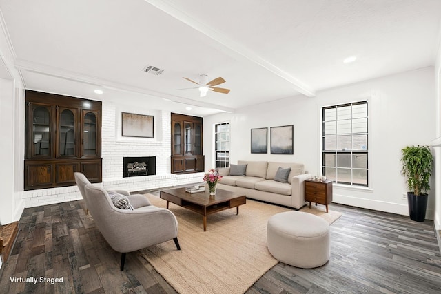 living area featuring wood finished floors, visible vents, baseboards, a brick fireplace, and beamed ceiling