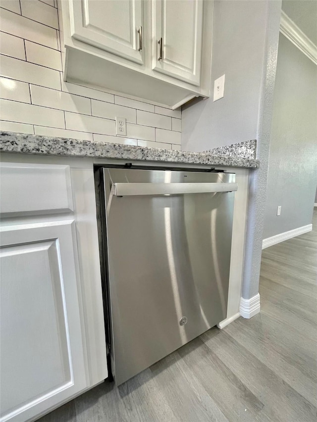 details with white cabinetry, backsplash, light stone counters, stainless steel dishwasher, and light wood-type flooring