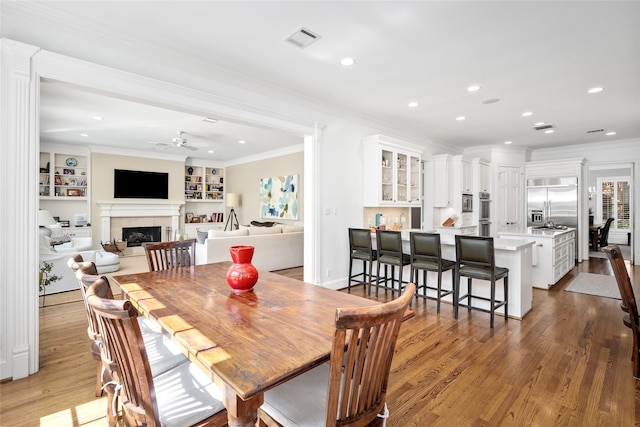 dining space featuring ornamental molding, a fireplace, wood finished floors, and visible vents