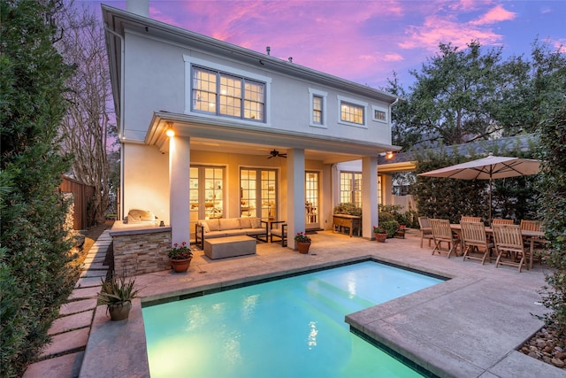 back of house at dusk featuring outdoor lounge area, fence, exterior kitchen, stucco siding, and a patio area