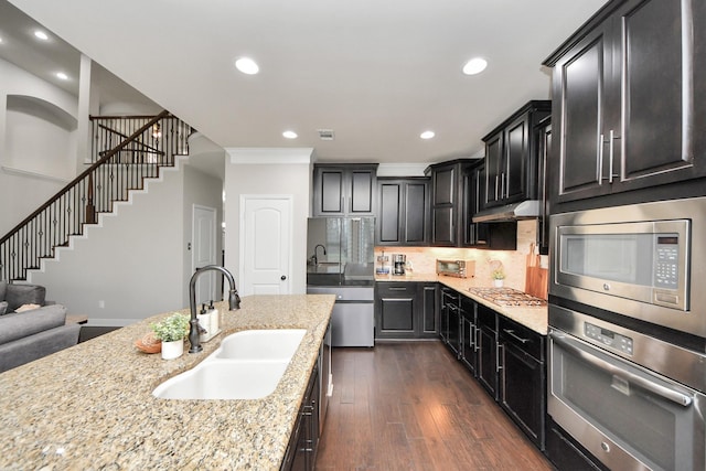 kitchen with sink, appliances with stainless steel finishes, light stone countertops, dark hardwood / wood-style flooring, and decorative backsplash