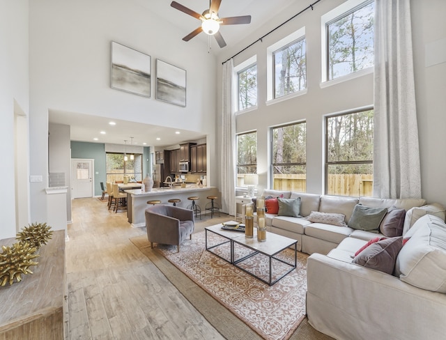 living area with a towering ceiling, light wood-style floors, ceiling fan, and recessed lighting