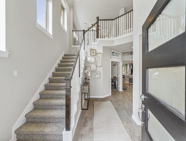 stairs with wood finished floors, a towering ceiling, and baseboards