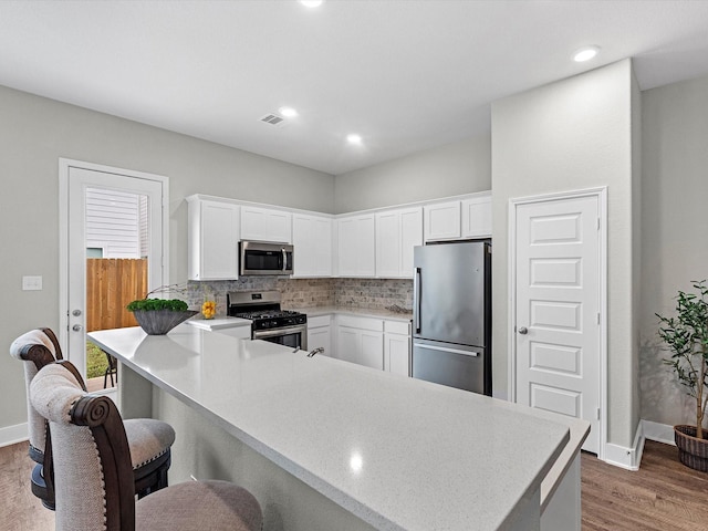 kitchen with white cabinets, backsplash, hardwood / wood-style flooring, kitchen peninsula, and stainless steel appliances