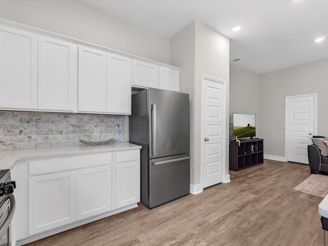 kitchen with stainless steel refrigerator, light hardwood / wood-style floors, decorative backsplash, and white cabinets