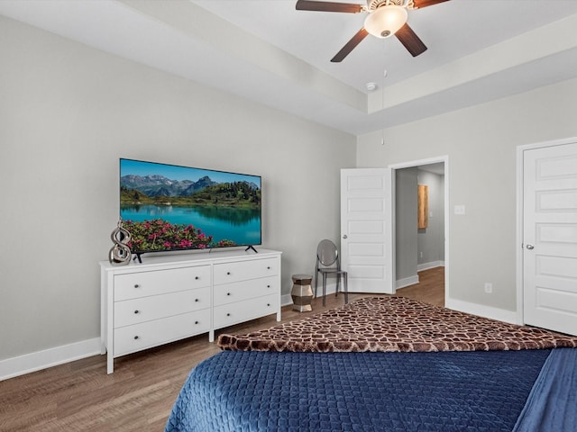 bedroom with a tray ceiling, wood-type flooring, and ceiling fan