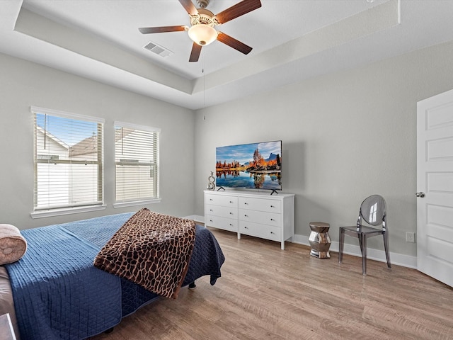 bedroom featuring a raised ceiling, ceiling fan, and light wood-type flooring