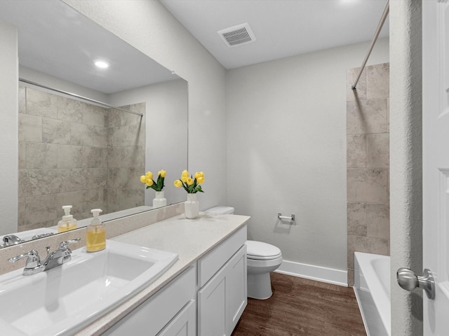 full bathroom with wood-type flooring, tiled shower / bath, vanity, and toilet