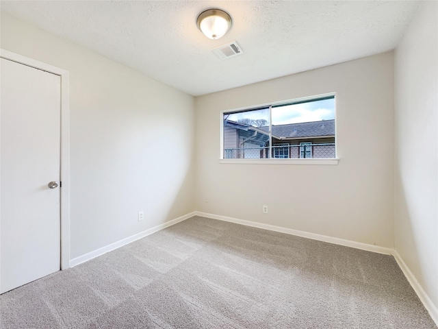 unfurnished room with a textured ceiling, carpet floors, visible vents, and baseboards